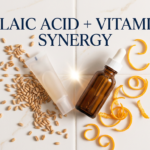 Azelaic acid tube and vitamin C serum converging on white tile surface with wheat and citrus props