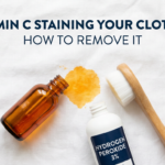 Vitamin C serum bottle tipped near yellow fabric stain with removal products on white linen