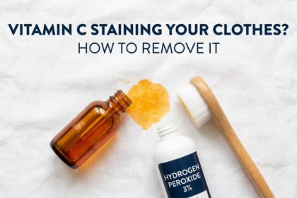 Vitamin C serum bottle tipped near yellow fabric stain with removal products on white linen