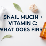 Snail mucin gel and vitamin C serum bottles with shell and leaf on white surface